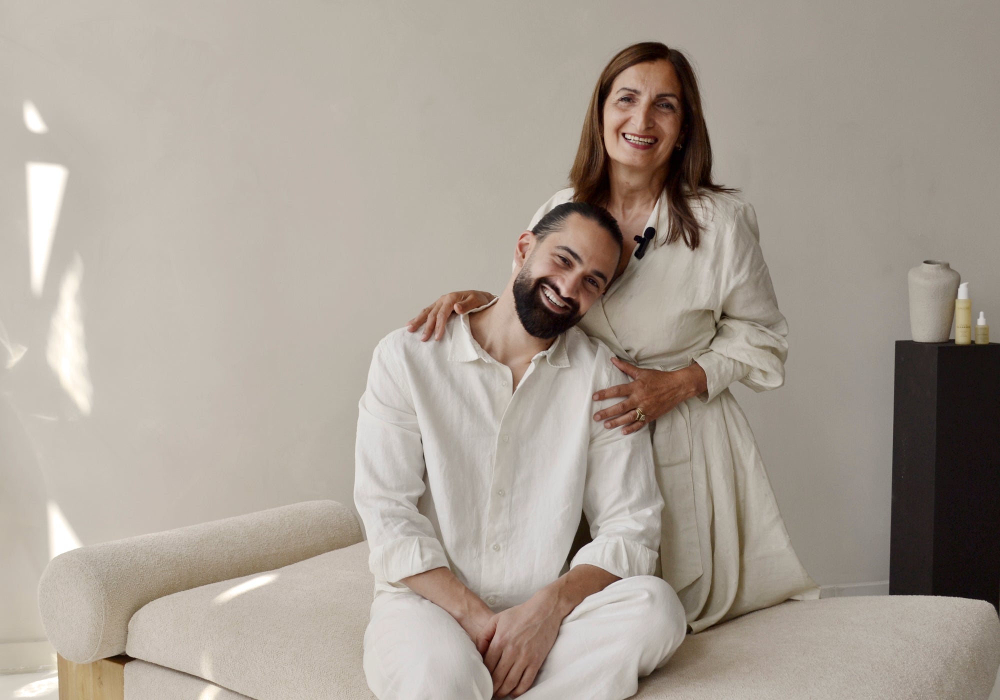 Man and woman in white outfits sitting on a couch in a minimalistic room.