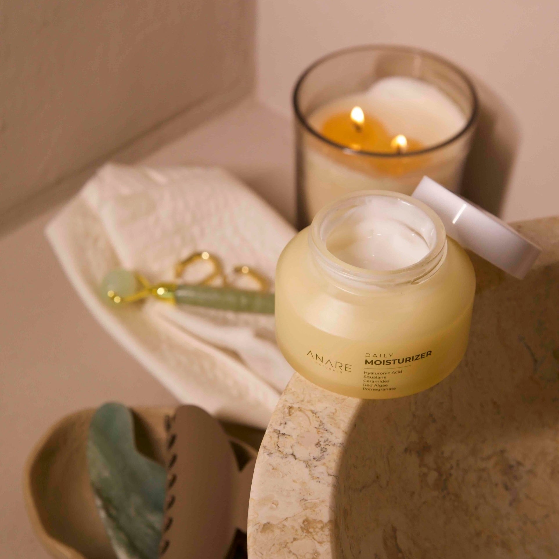 Bottle of Anare Daily Moisturizer on a bathroom counter with a lit candle and washcloth in the background