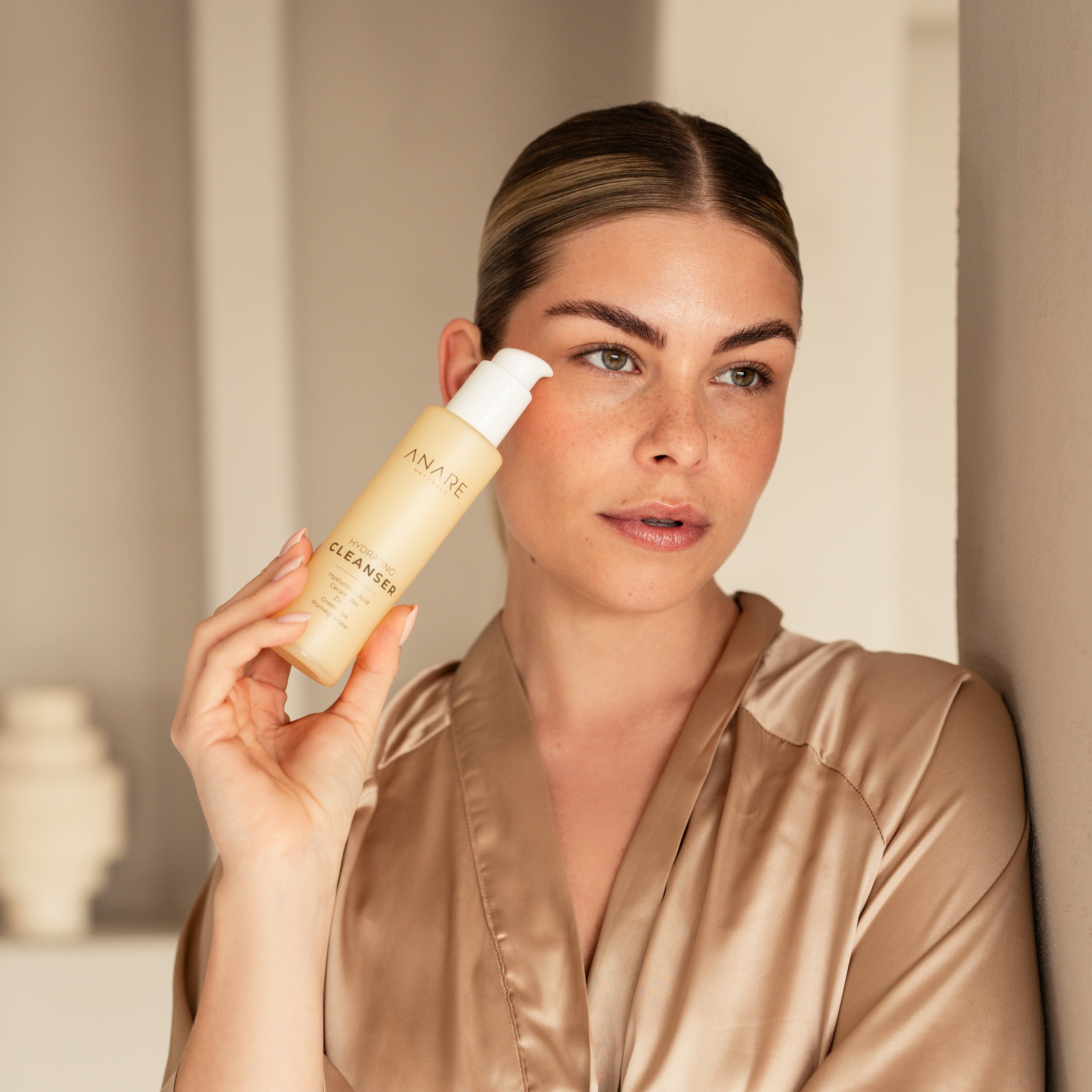 Model holding Anare Hydrating Cleanser bottle