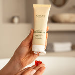 Hand holding a tube of ANARE Gentle Exfoliator with a blurred bathroom background