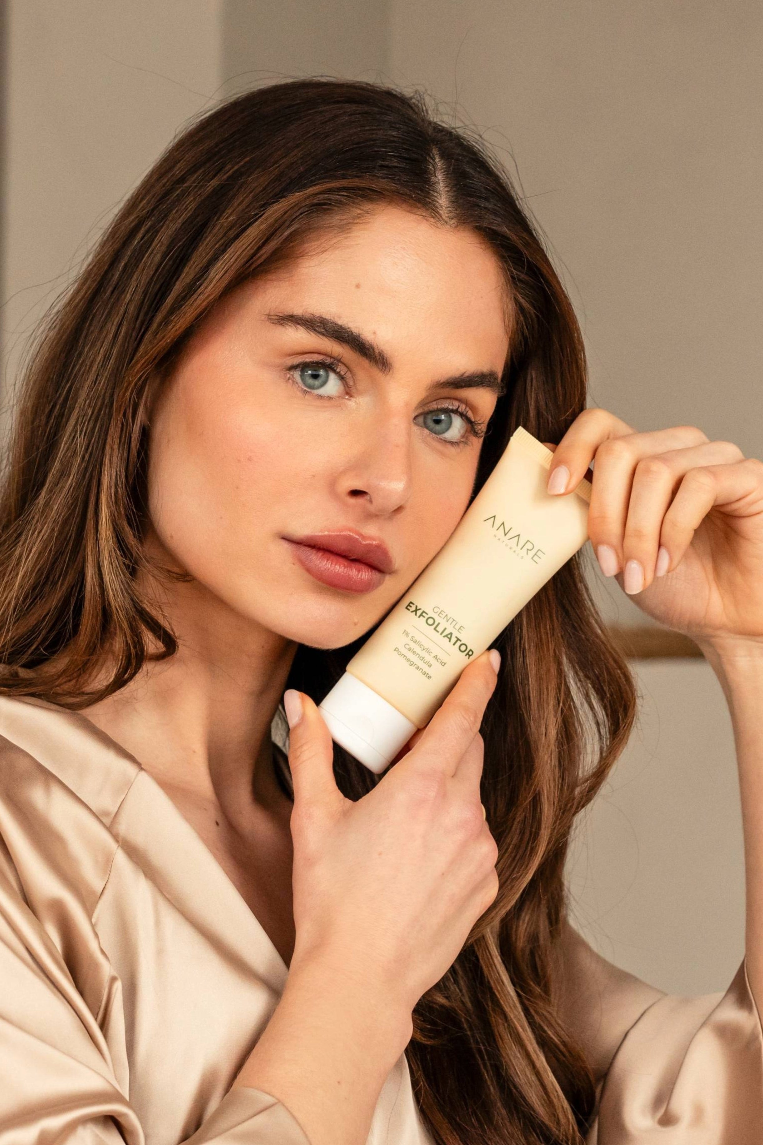 Model with blue eyes and brown hair holding Anare Naturals gentle exfoliator, showcasing the product.