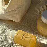 Yellow Vitamin C Serum bottle and other skincare products on light color cloth in sunlight