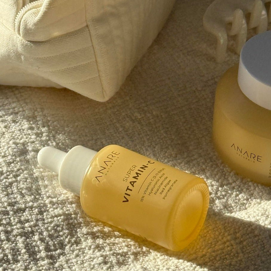 Yellow Vitamin C Serum bottle and other skincare products on light color cloth in sunlight